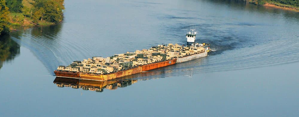 Tugboat pushing barge with army trucks