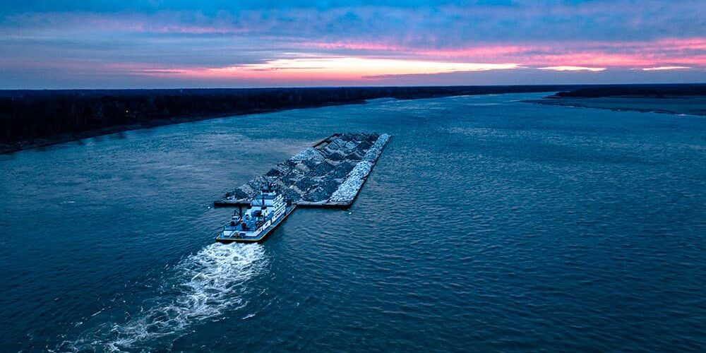 overview head view of tug pushing barge of rock down the river